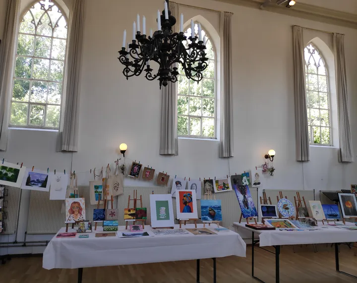 Werk van cursisten op tafels in een kerkzaal, expositie 2024